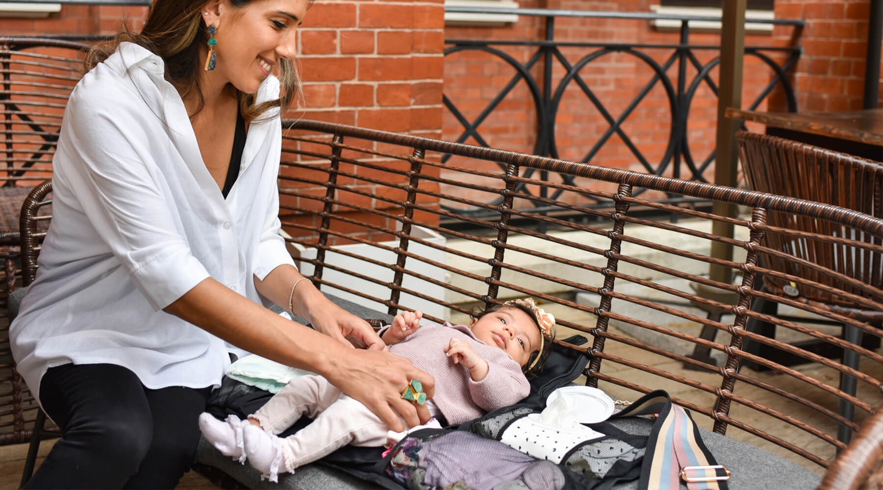Mom changing her baby on a diaper bag that opens to changing station on a bench